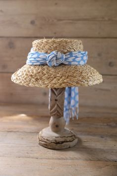 a straw hat on top of a wooden stand with blue and white polka dot ribbon