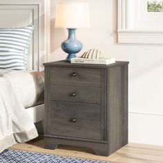 a night stand with two drawers and a lamp next to it on top of a bed