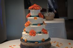 a three tiered wedding cake with orange flowers on the top and bottom, sitting on a table