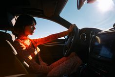 a woman sitting in the driver's seat of a car with her hand on the steering wheel