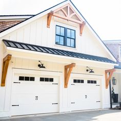 Farmhouse garage LED lighting from Barn Light Electric Outdoor Light Above Garage, Awning Above Garage Door, Farmhouse Exterior Lighting Garage, Decorative Garage Overhang, White Garage With Wood Doors, White And Black House Exterior With Wood, Pergola Over Garage Door Wood, Garage Awnings Exterior, Exterior Lights Above Garage Doors