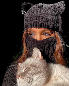 a woman wearing a knitted hat and scarf with a cat sleeping on her chest