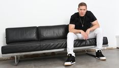 a man sitting on top of a black couch in front of a white wall and floor