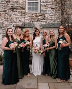 a group of women standing next to each other in front of a stone building holding bouquets