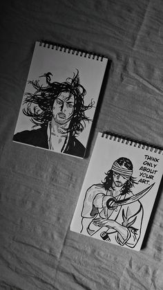 two notebooks with drawings on them sitting on a bed next to eachother