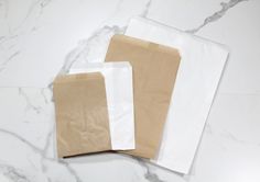 two brown and white paper bags sitting on top of a marble countertop next to each other