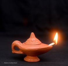 a small clay oil lamp with a lit candle in the middle on a black background