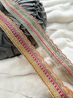 several different colored ribbons laying on top of a white bed sheet with a pillow in the background