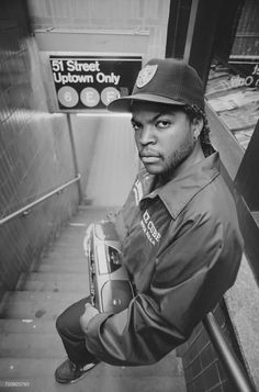 a man in a hat and jacket standing on the stairs with his arms folded up