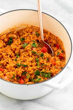 a pot filled with rice and vegetables on top of a white tablecloth next to a spoon