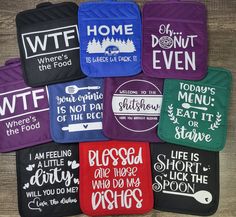 six oven mitts with sayings on them sitting on a wooden surface in different colors