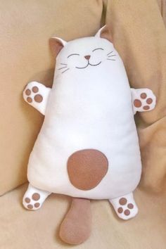 a white cat stuffed animal laying on top of a bed with brown and white pillows