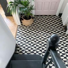 a black and white tiled floor with a potted plant next to the stair railing