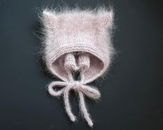 a knitted hat with a bow on the front and side, sitting on a black surface