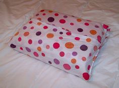 a polka dot pillow on a bed with white sheets and pink linens that has orange, purple, and red dots