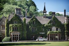 an old house covered in ivy with people walking by it and cars parked outside the building