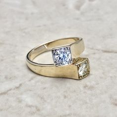 two yellow gold rings with white diamonds on a marble surface, one has a square cut diamond in the middle