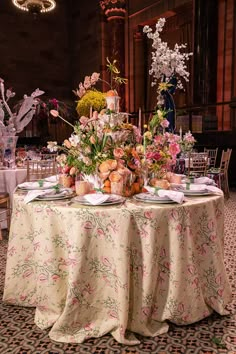 a table with flowers and plates on it in a large room filled with tables cloths