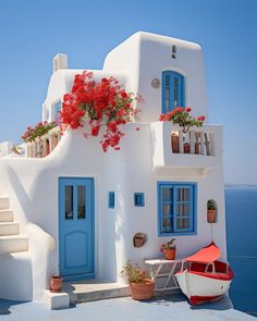 a white house with blue doors and red flowers on the windows is next to a boat