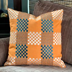 an orange and blue pillow sitting on top of a brown couch next to a window