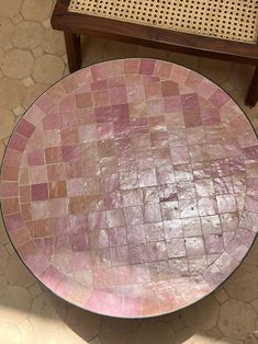 a pink and brown mosaic table sitting on top of a tiled floor next to a chair