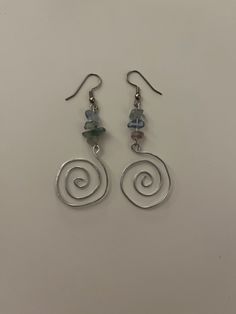 two silver spiral earrings with blue and green beads hanging from the ear wires on a white surface