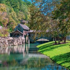 a river running through a lush green forest next to a stone covered bridge with a wooden structure on top