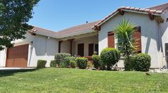 a house that is in the grass with trees and bushes around it on a sunny day