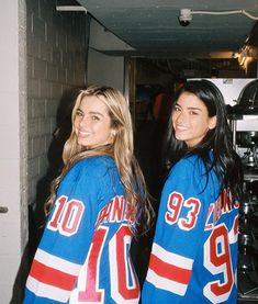 two women in blue hockey jerseys standing next to each other and smiling at the camera