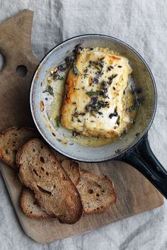 a pan filled with bread and cheese on top of a cutting board next to slices of bread