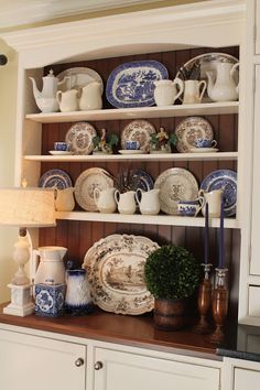 an old china cabinet with blue and white dishes on it's shelves, next to a lamp