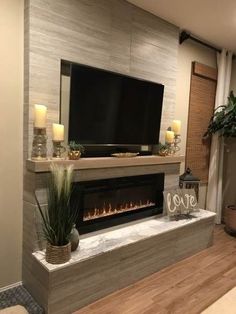 a living room with a fireplace and television on top of the mantel, surrounded by candles