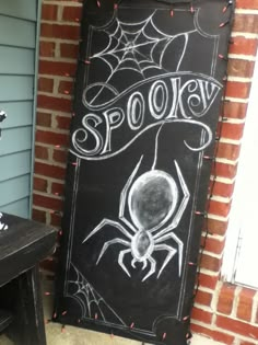 a chalkboard sign that says spooky with a spider drawn on it in front of a brick building