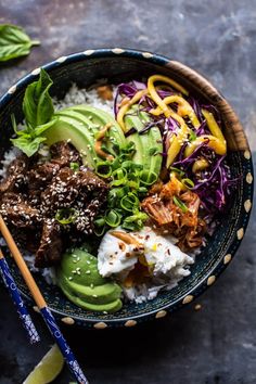 a bowl filled with rice, meat and veggies next to chopsticks