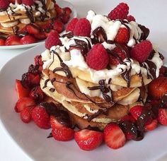 two white plates topped with pancakes covered in whipped cream and strawberries