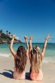 two women sitting on the beach with their hands in the air