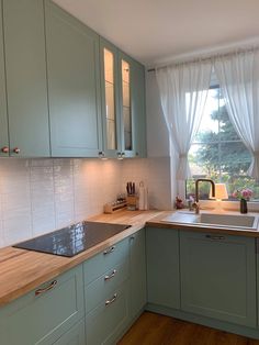 a kitchen with green cabinets and white curtains on the window sill above the sink