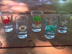 four shot glasses sitting on top of a wooden table covered in sand and seashells