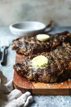 two steaks with butter on a wooden cutting board