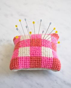 a pink and white pillow with pins in it on a marble counter top next to a pin cushion