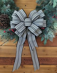 a black and white striped bow hanging on a wooden wall with pine cones, berries and evergreens