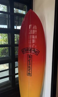 a red and yellow surfboard sitting next to a window