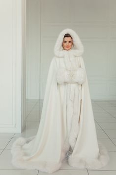 a woman in a white gown and fur coat standing on the floor with her arms crossed