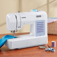 a white sewing machine sitting on top of a wooden table next to scissors and thread