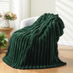 a large green blanket sitting on top of a wooden floor next to a white chair