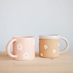 two coffee mugs sitting next to each other on a wooden table with flowers painted on them