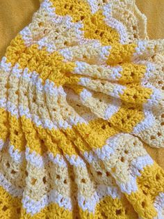 a yellow and white crocheted blanket laying on top of a bed