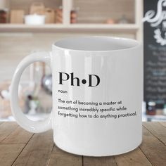 a white coffee mug with the words ph d on it sitting on a wooden table