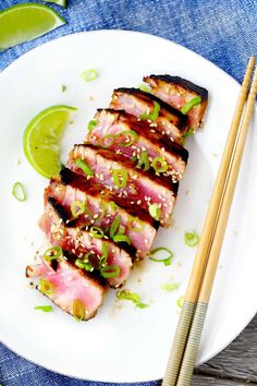 a white plate topped with meat and chopsticks next to a lime wedge on top of a wooden table