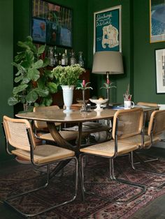 a dining room with green walls and wooden table surrounded by chairs, potted plants and pictures on the wall